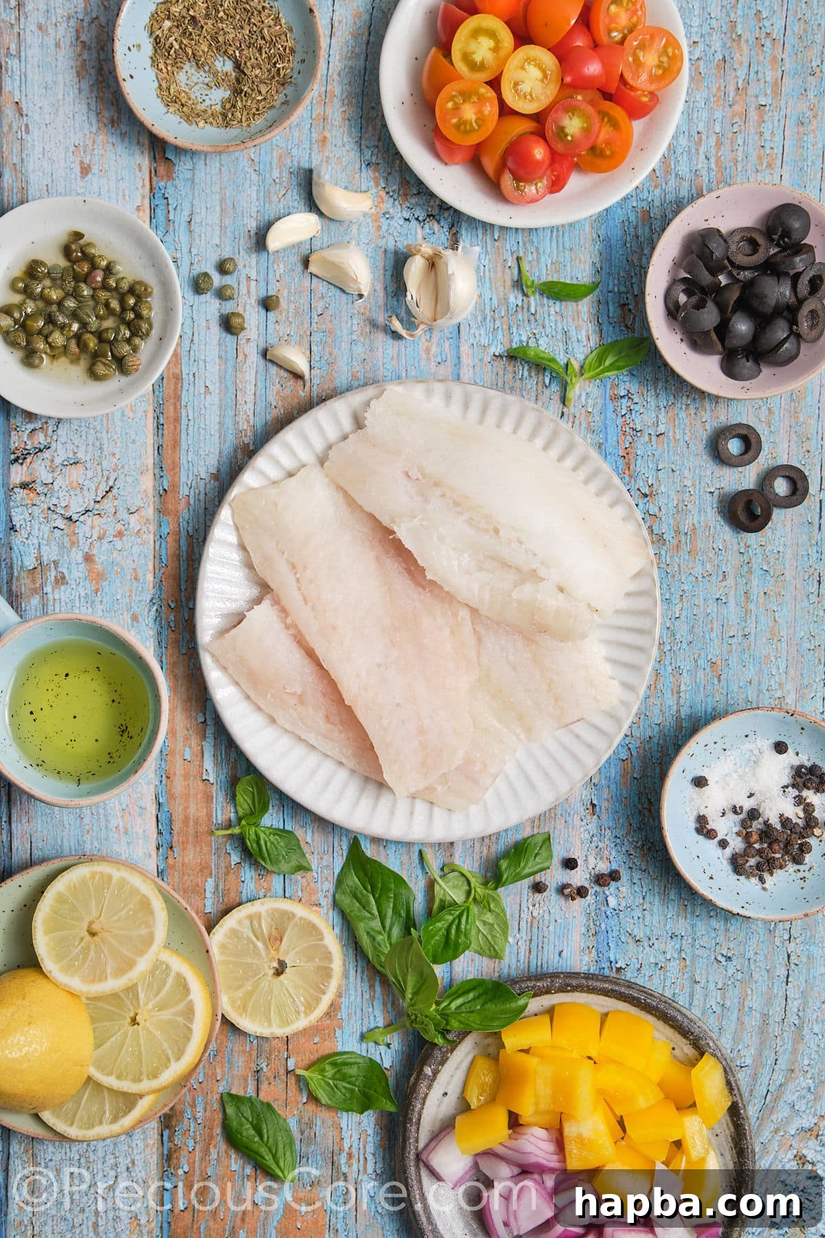A flat lay photograph showcasing all the fresh ingredients needed for the baked Mediterranean fish recipe, including cod fillets, various vegetables, herbs, and olive oil.