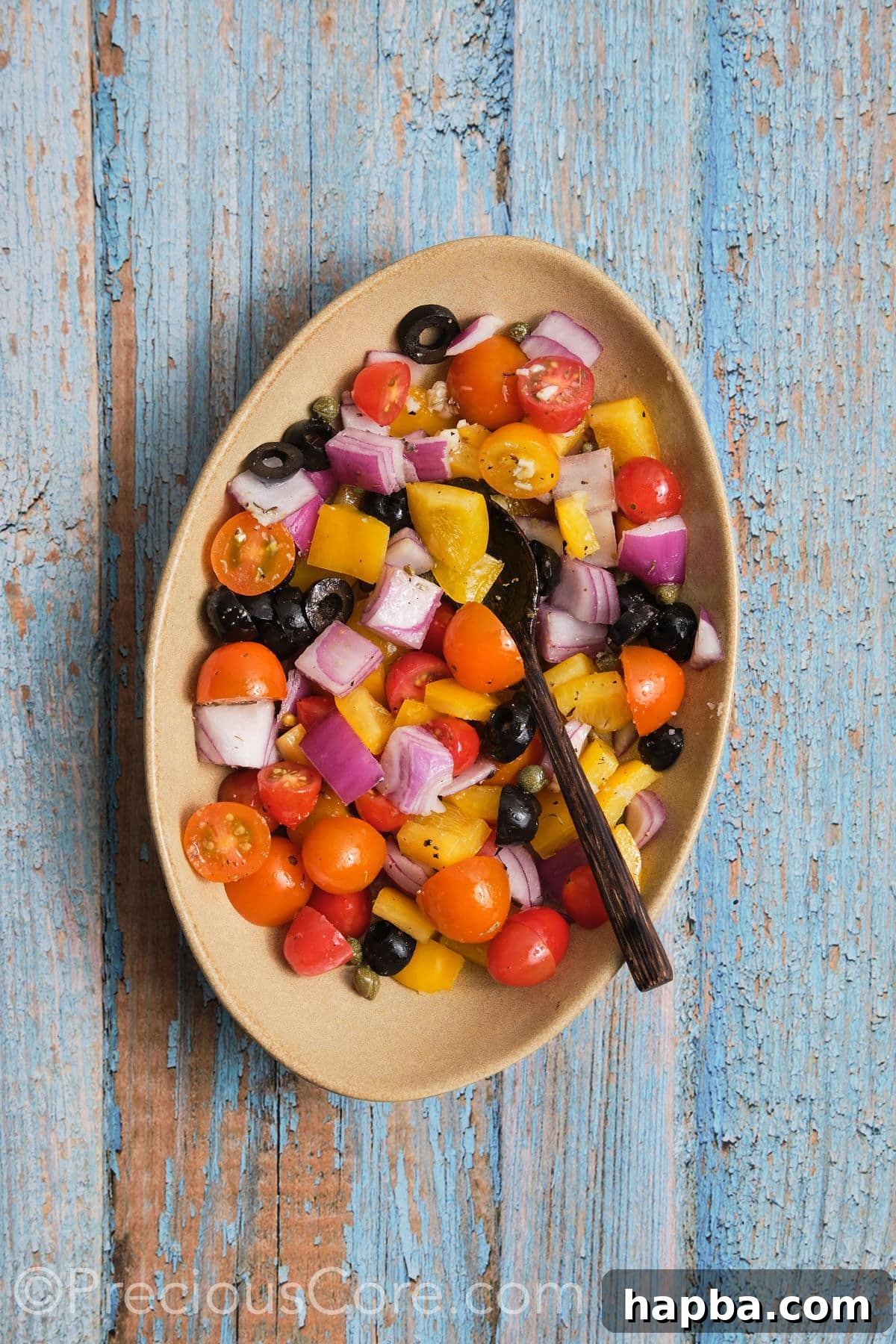 A bowl filled with diced vegetables—bell peppers, red onions, cherry tomatoes, black olives, and capers—all coated in olive oil and seasonings, ready for baking.
