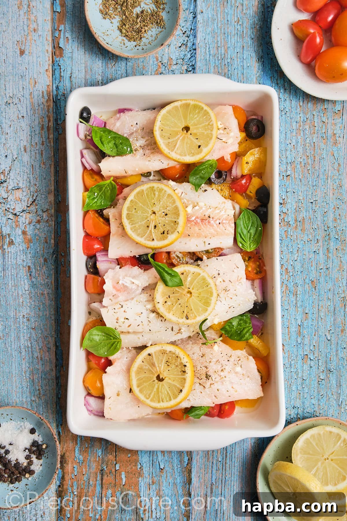 A baking dish filled with the colorful medley of chopped vegetables, topped with perfectly arranged marinated fish fillets and thin lemon slices, ready for the oven.