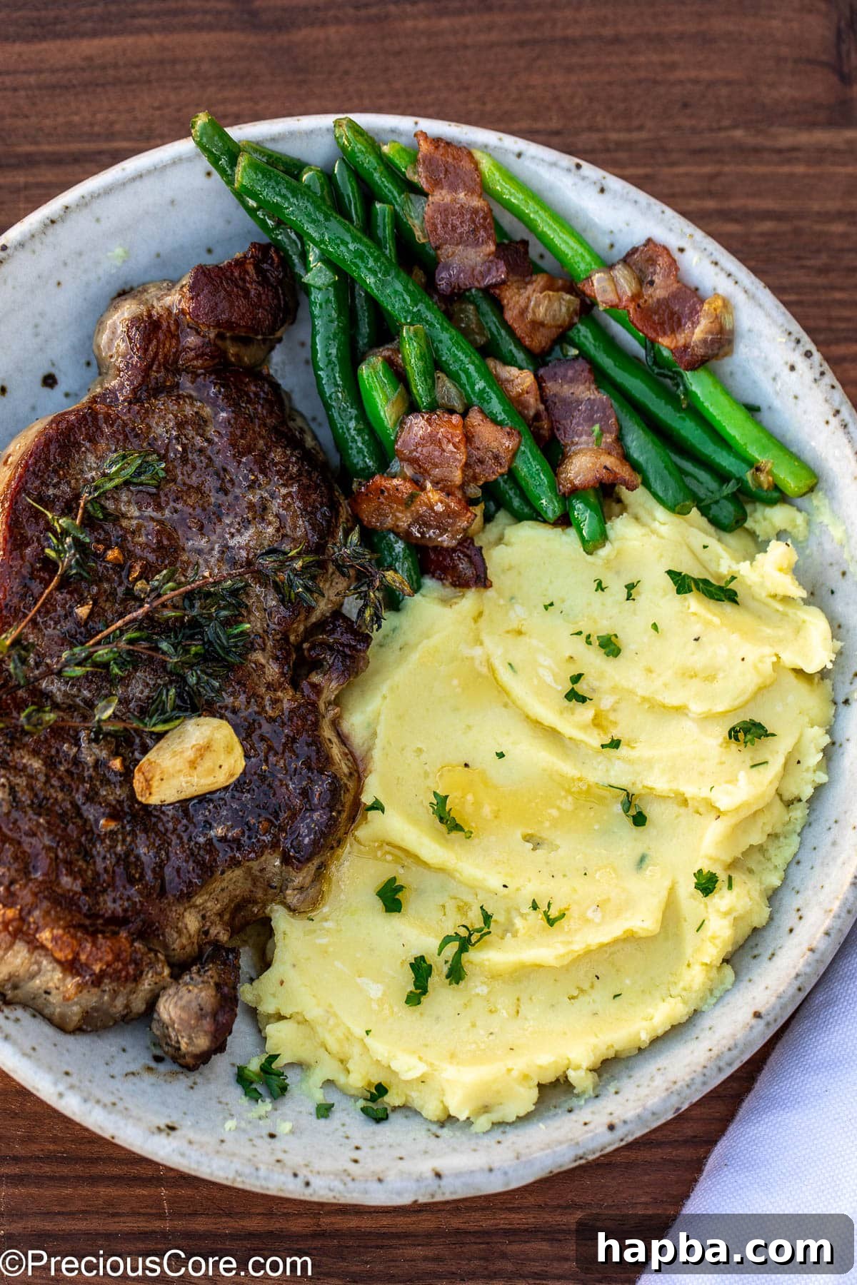 Bacon green beans served alongside a juicy steak and creamy mashed potatoes for a complete meal.