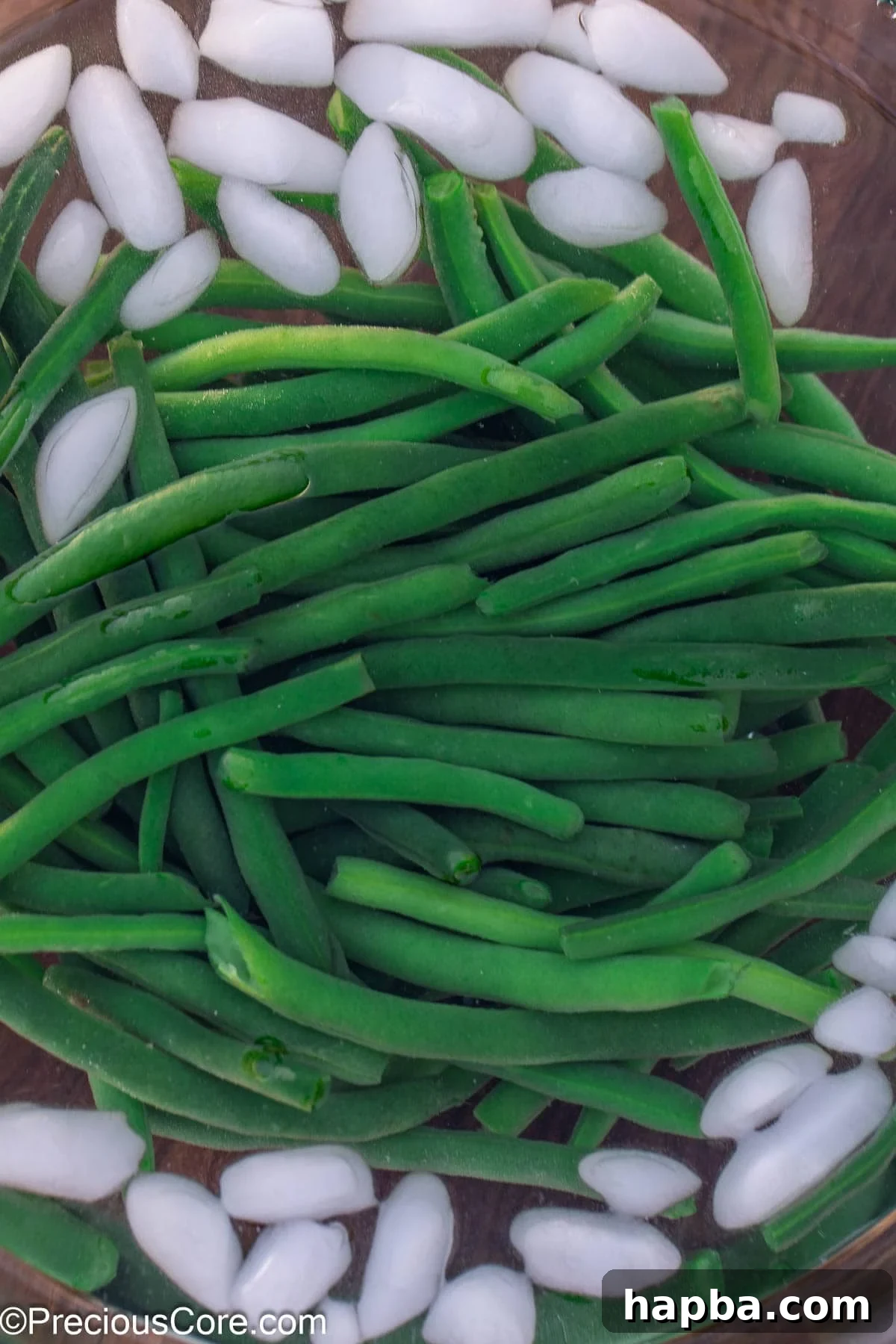 Blanched green beans cooling rapidly in a bowl of ice water.