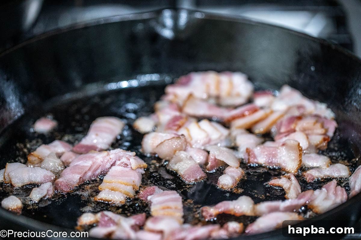 Chopped bacon sizzling and crisping in a hot skillet.