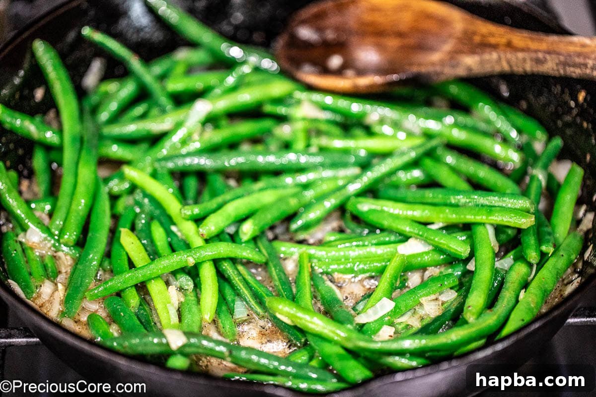 Green beans added to the skillet, tossed with onions and spices.