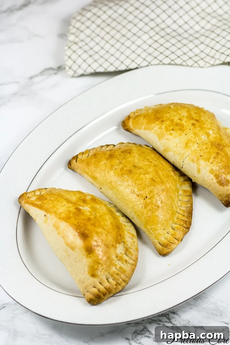Three golden-brown African meat pies resting on a white platter, showcasing their flaky crust and inviting appearance.