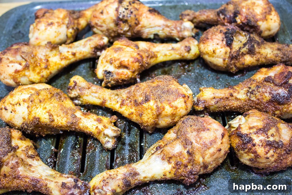 Close-up of golden brown grilled chicken drumsticks on a broiling pan, garnished with herbs.