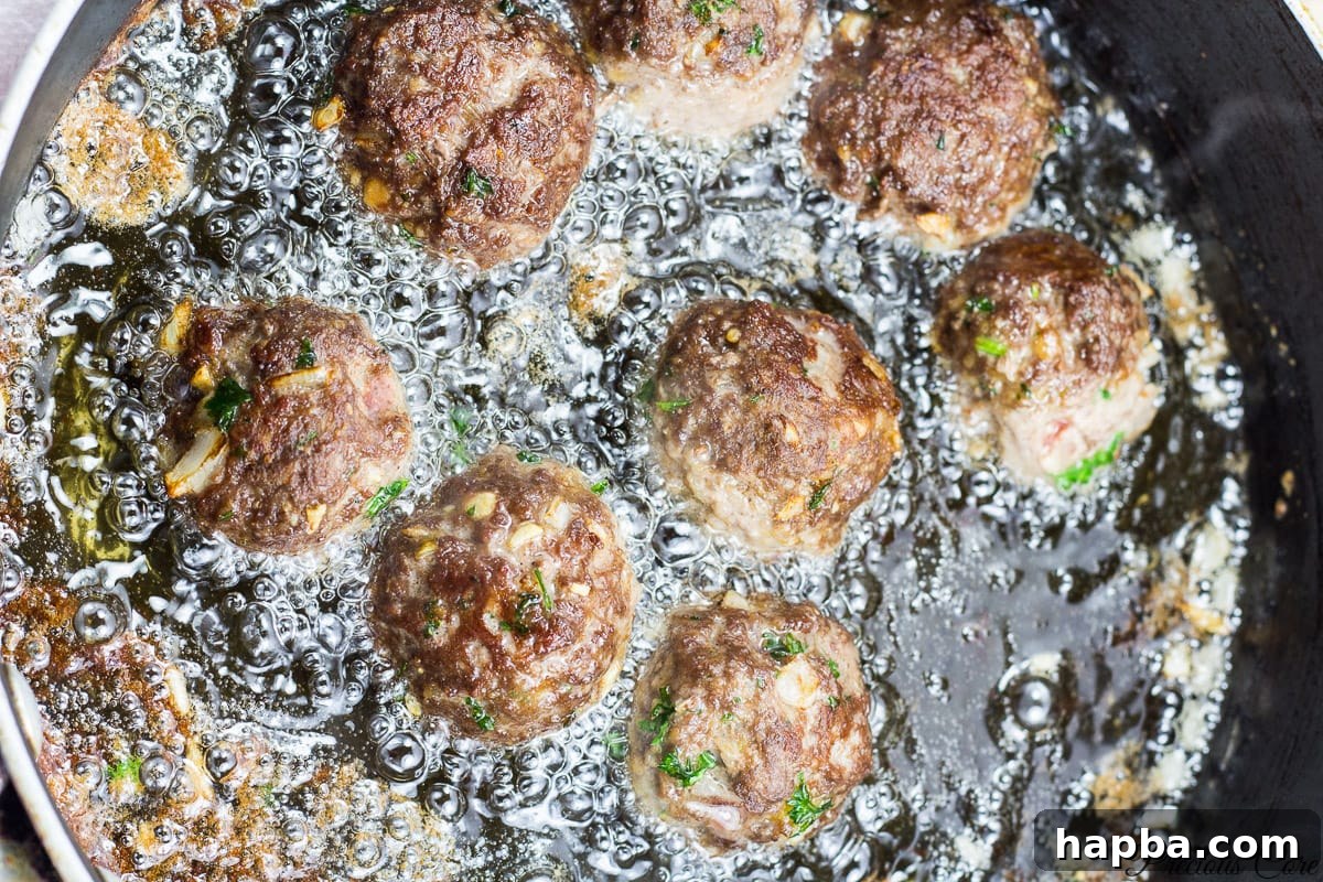 African Spiced Meatballs 8 Meatballs sizzling and browning in hot oil in a frying pan.