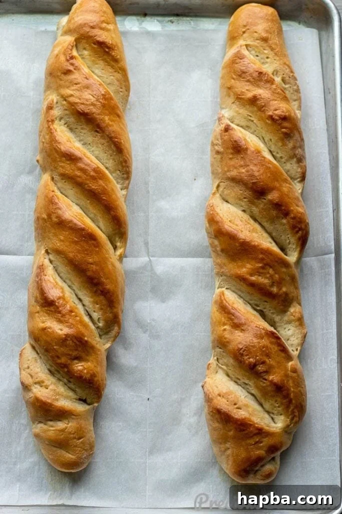 Several finished French bread loaves on a large baking sheet, glistening with melted butter