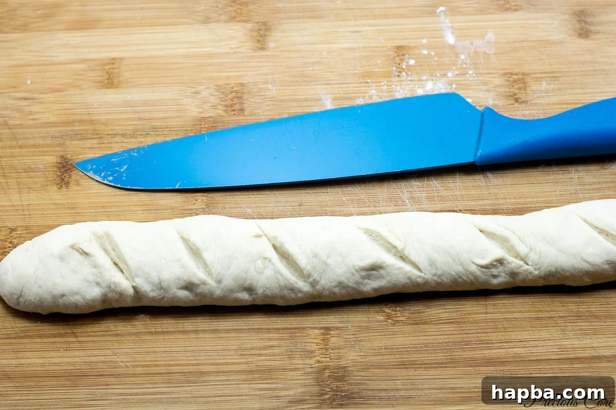 French bread loaf with diagonal scores on top, prepared for proofing