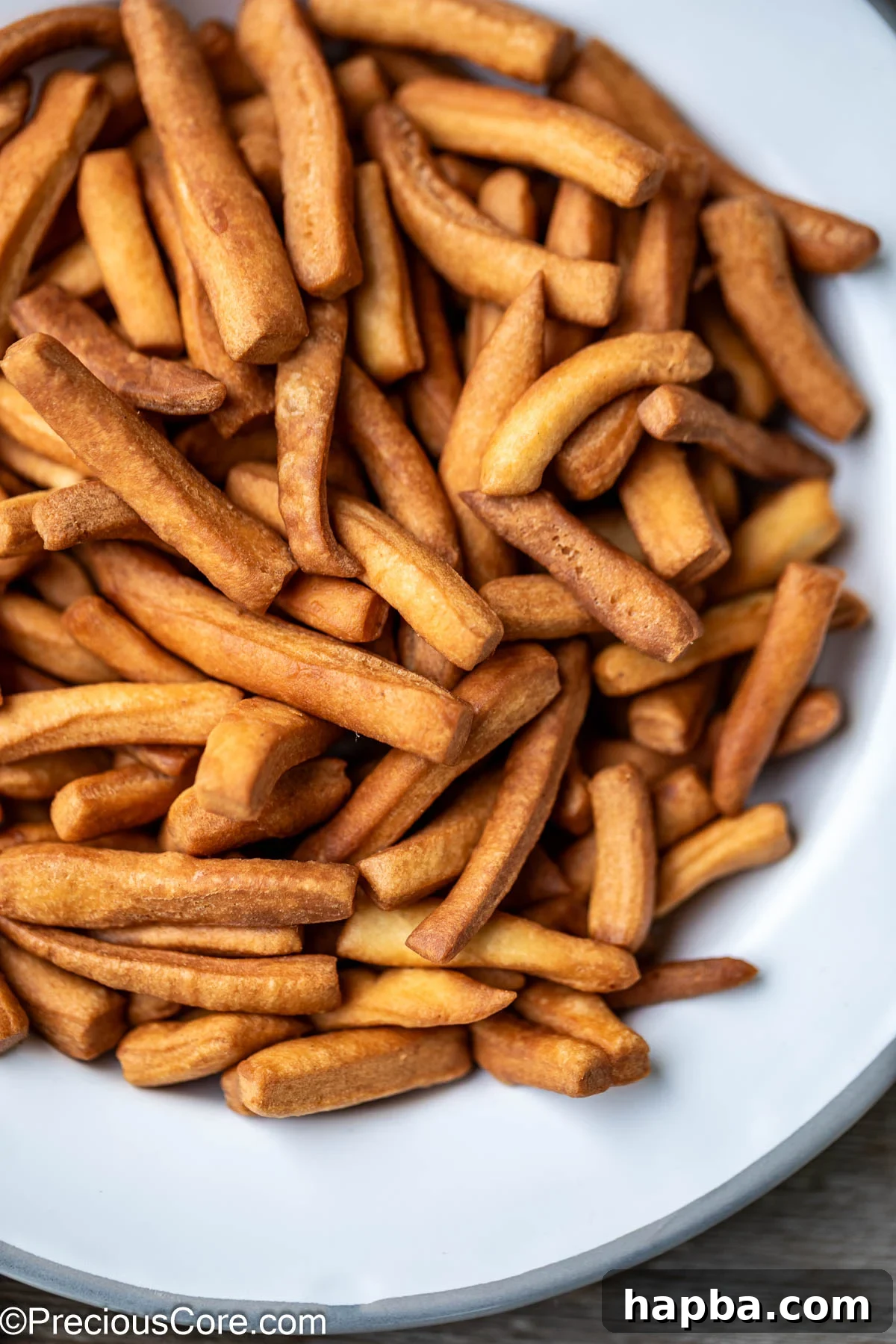 Close up of a pile of golden-brown Chin Chin pieces on a white plate, ready to be eaten.
