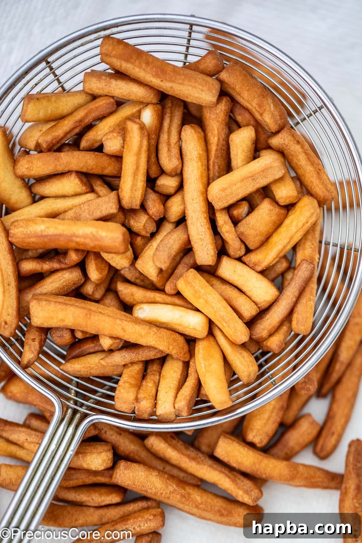 Crunchy Chin Chin pieces being scooped out of frying oil with a slotted spoon.