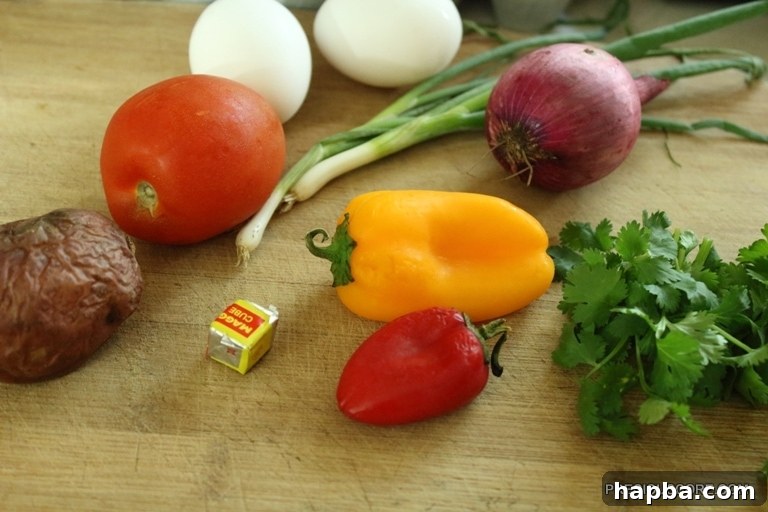 Ingredients laid out: baked potato, bell peppers, onions, eggs, tomato, seasoning cube, and cilantro.