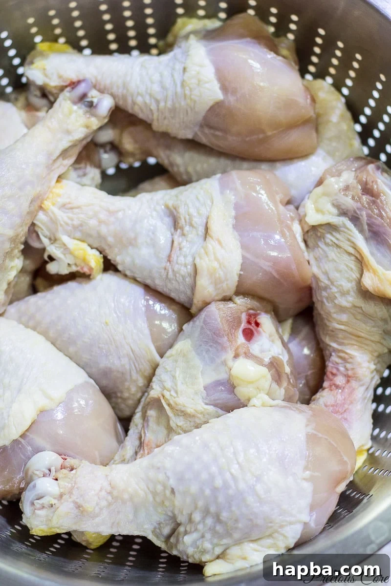 Fresh chicken drumsticks ready for seasoning in a porous pan, emphasizing preparation for oven grilling.