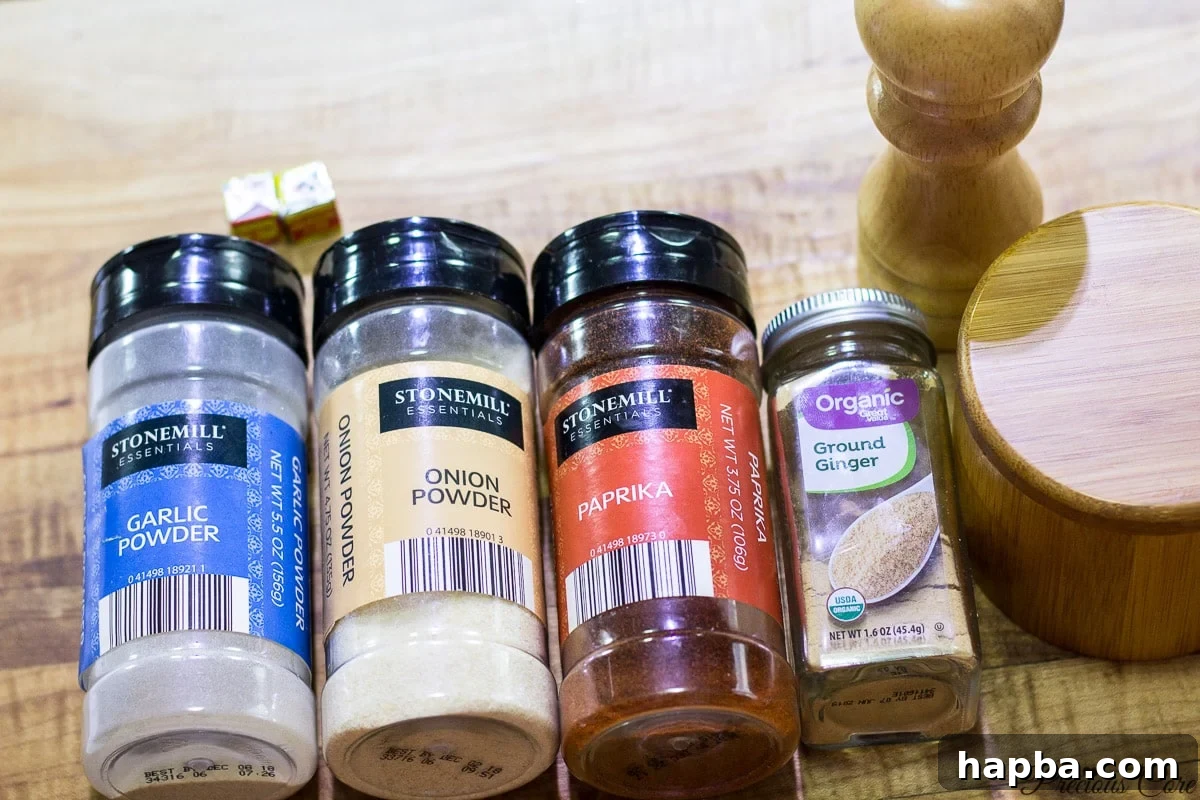 An array of dried spices and seasonings, including garlic powder, ginger, paprika, onion powder, and Maggi cubes, laid out for a chicken marinade.