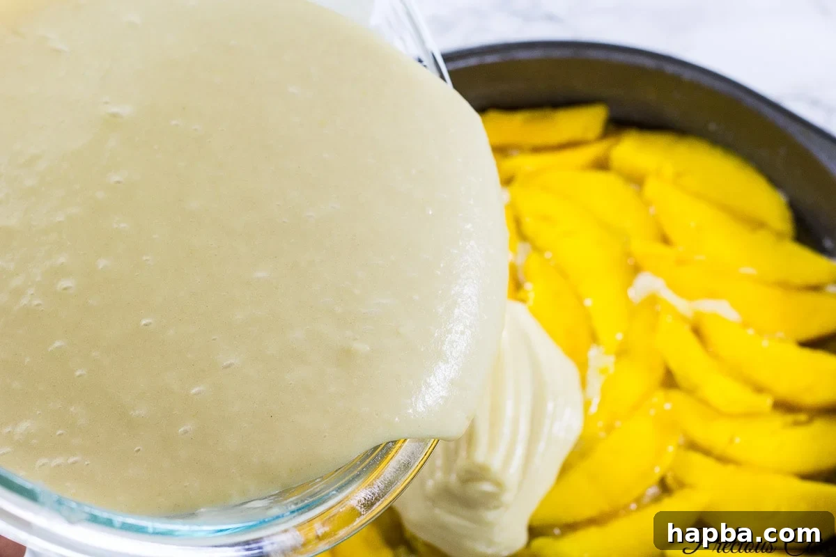 Tropical Mango Delight Cake 6 Smooth cake batter being poured gently over a layer of sliced mangoes in a baking pan