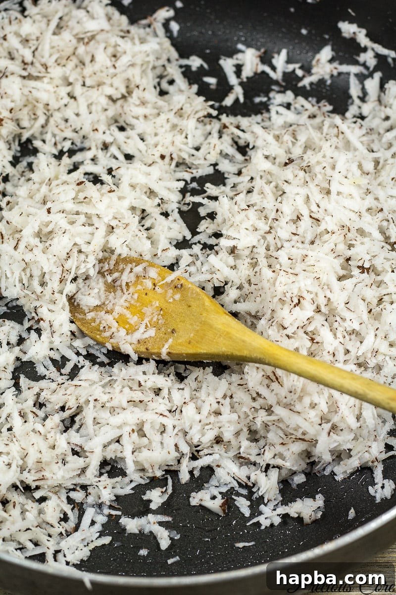 A non-stick pan on a stovetop, with shredded coconut being stirred into a sugar and water mixture, marking the initial step of making Coconut Sweet.