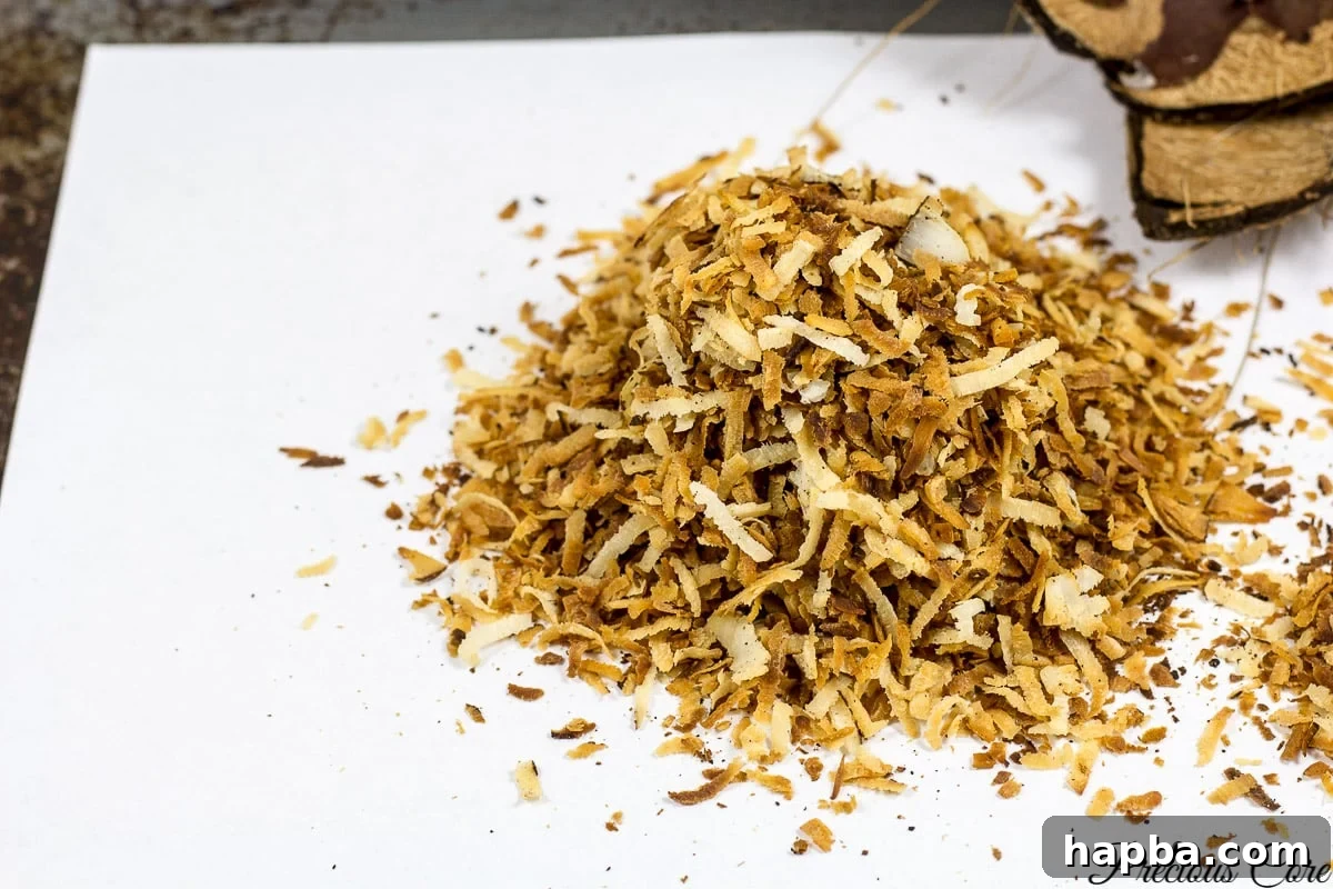 A close-up of golden-brown toasted coconut flakes resting on a sheet of parchment paper.