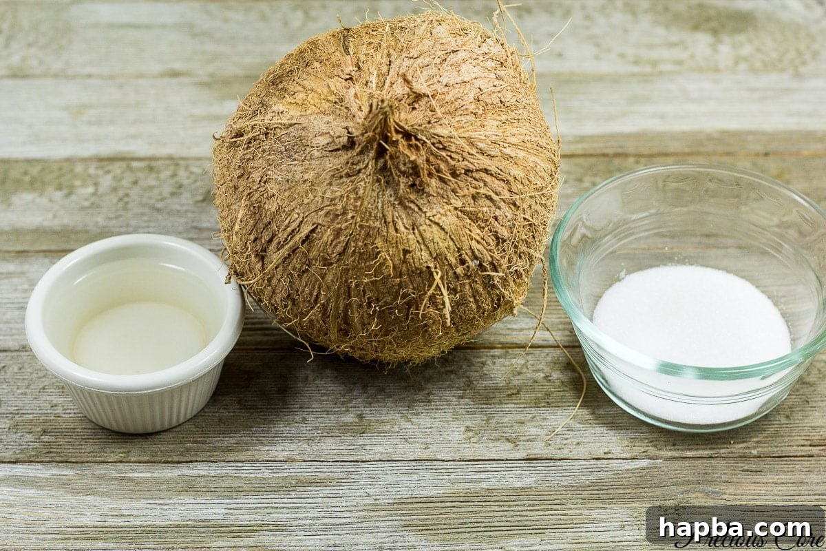 The three essential ingredients for Coconut Sweet: a fresh whole coconut, granulated sugar, and water, laid out on a kitchen surface.