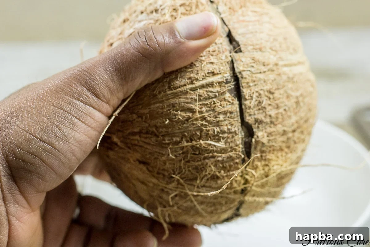 A freshly cracked coconut, with clear coconut water collected in a bowl, demonstrating a successful opening.