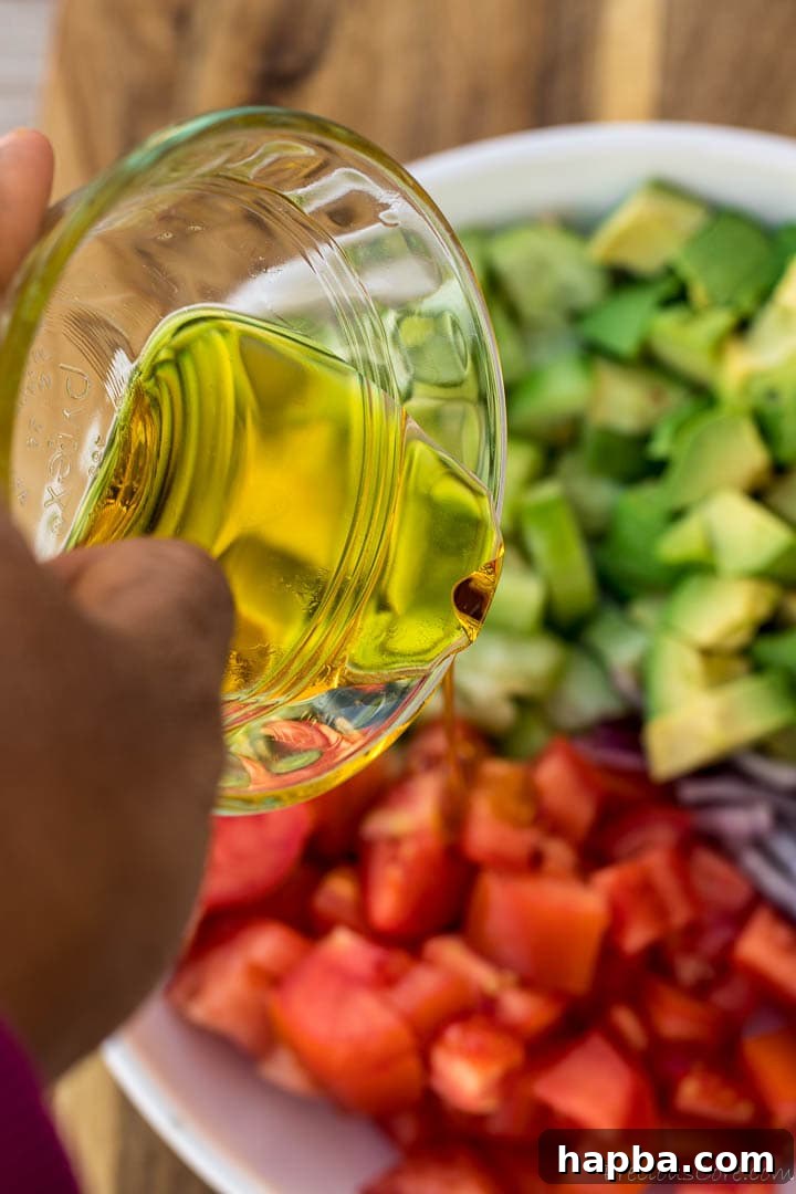 Hand holding a bowl of olive oil and pouring over avocado salad.