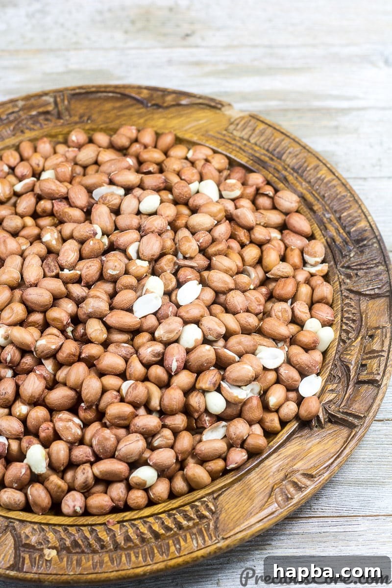 Three cups of raw, shelled groundnuts (peanuts) displayed in a traditional wooden bowl, ready for roasting.