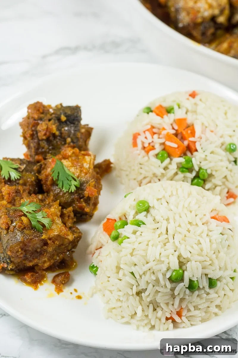 Sweet Heat Fish 6 A close-up of Nigerian Peppered Fish served with a side of white rice, showcasing the vibrant red sauce and flaky fish texture.
