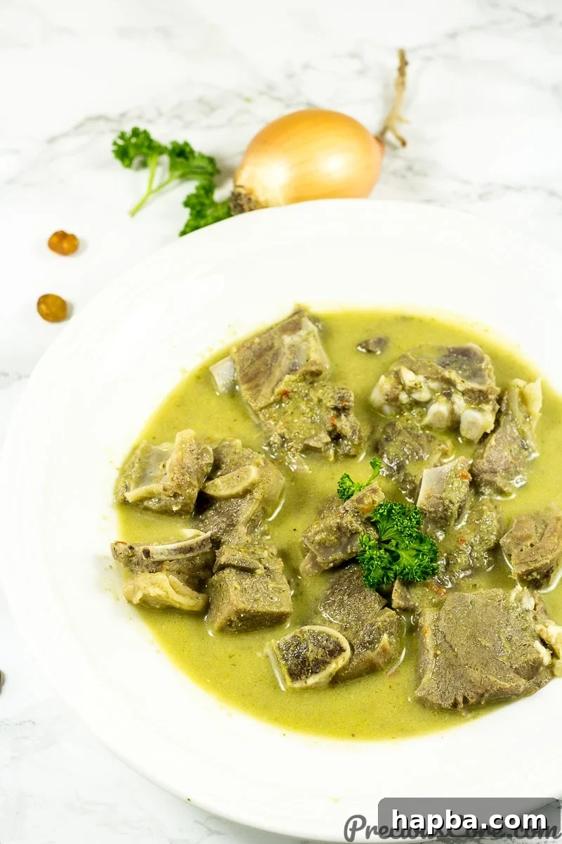 A bowl of Nigerian goat meat pepper soup, garnished with herbs.