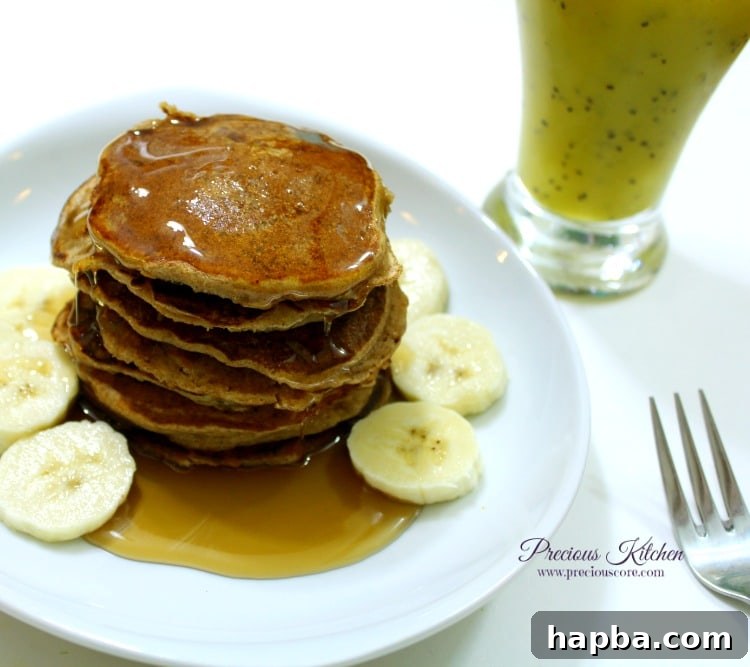 Stack of fluffy whole wheat banana pancakes topped with honey and fresh fruit, served with a smoothie