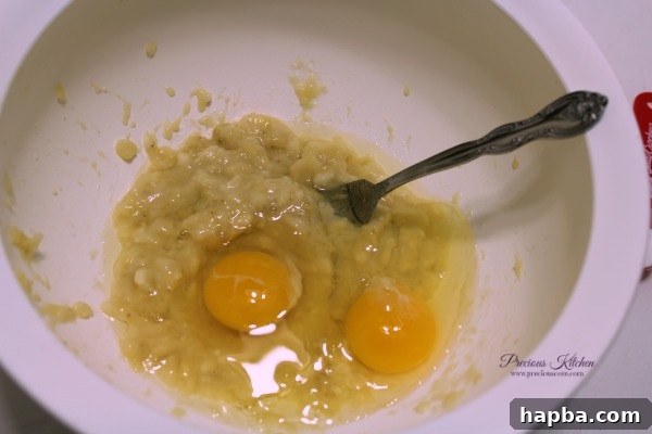 Cracked eggs being added to the mashed bananas in a bowl