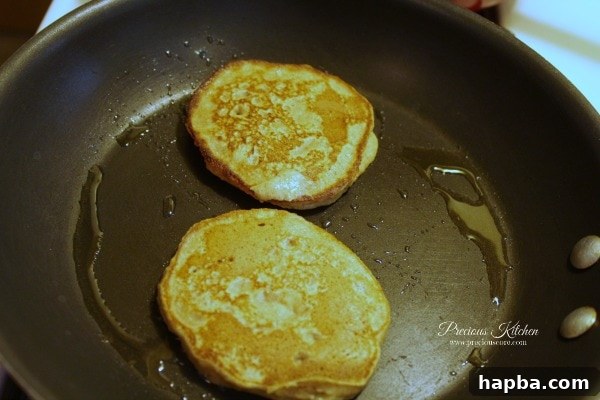 Whole wheat banana pancakes being flipped on a frying pan to cook the second side