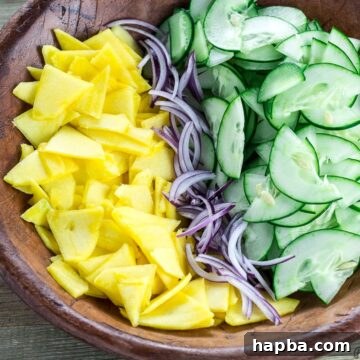 Sliced cucumber, mango and onion in a bowl, ready to be dressed.
