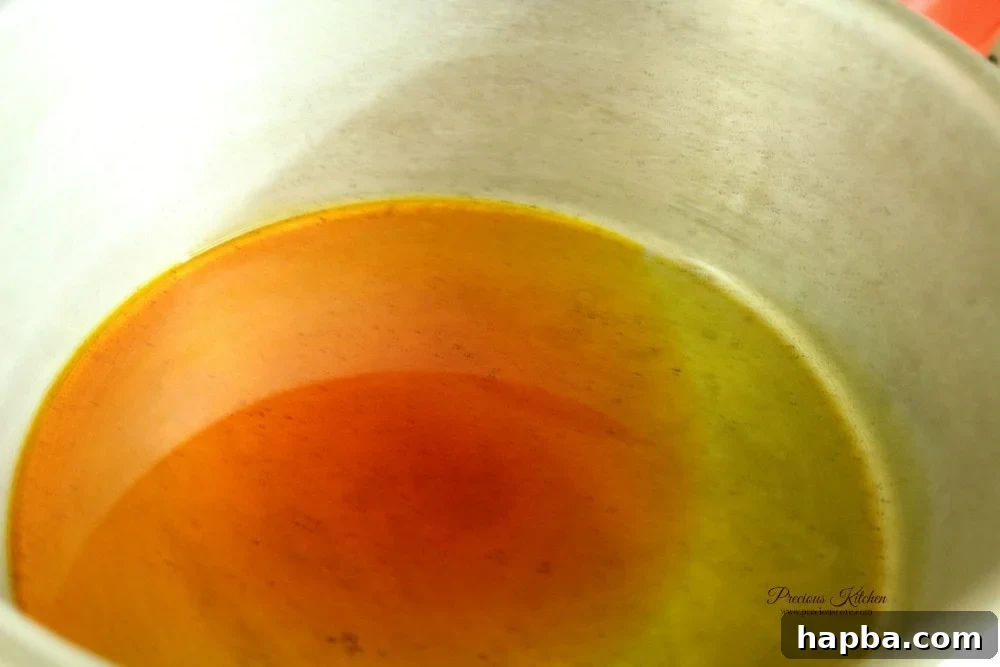Red palm oil heating in a pot, preparing the aromatic base for Tukuni / Pomme Pilées.