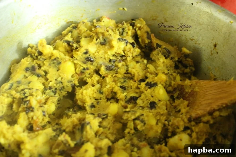 Mashing the boiled potatoes and beans with a wooden spoon into the flavorful palm oil and spice mixture to create creamy Tukuni.