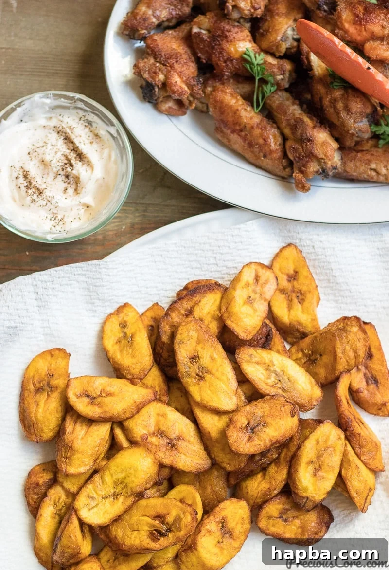 Fried plantains served with chicken wings on a white plate.