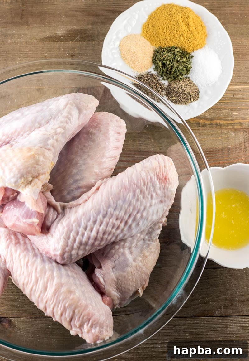 A selection of fresh turkey wings in a bowl, various dried spices and herbs arranged on a plate, and a small bowl of melted butter.