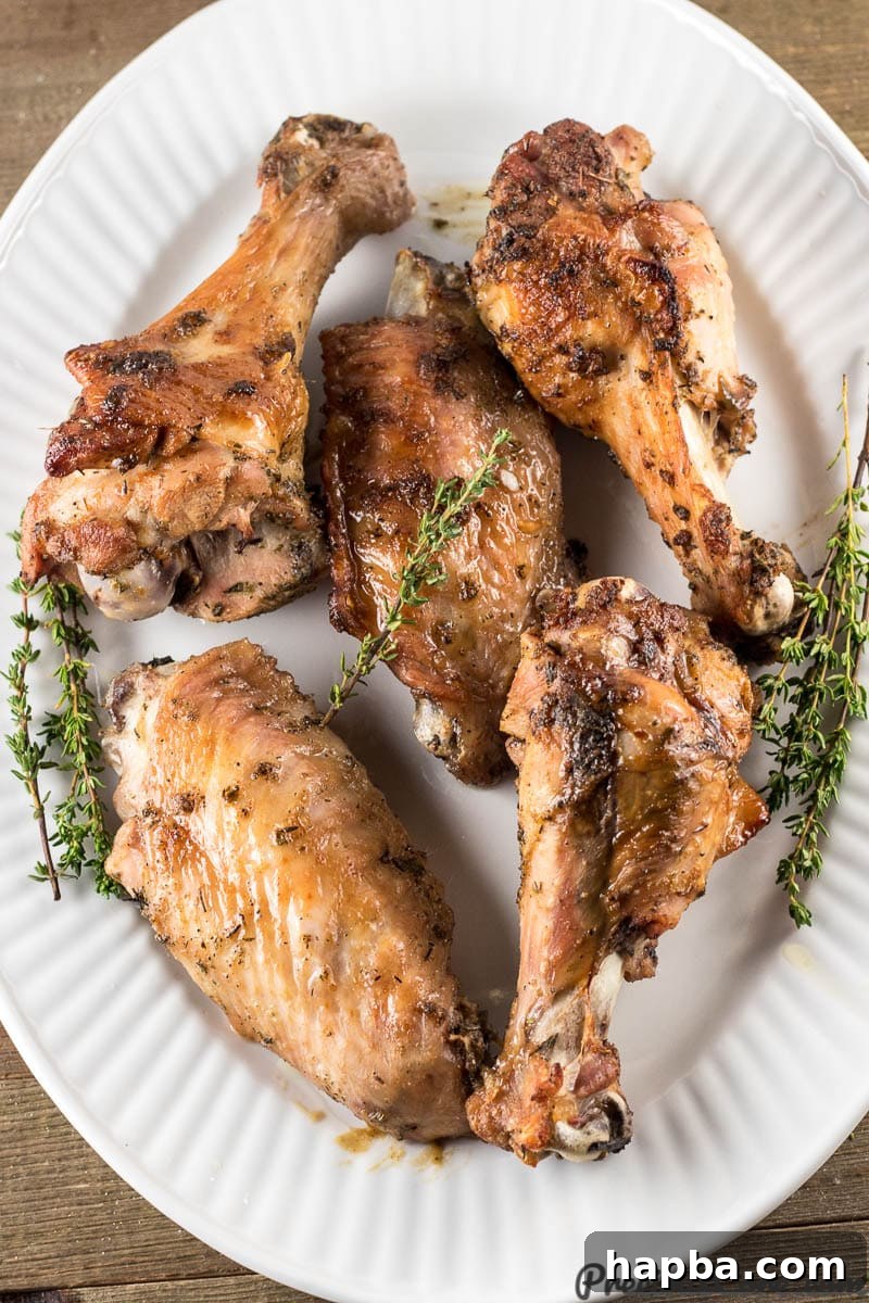 A large white platter presenting a generous serving of freshly baked, golden-brown turkey wings, lightly garnished with fresh herbs.