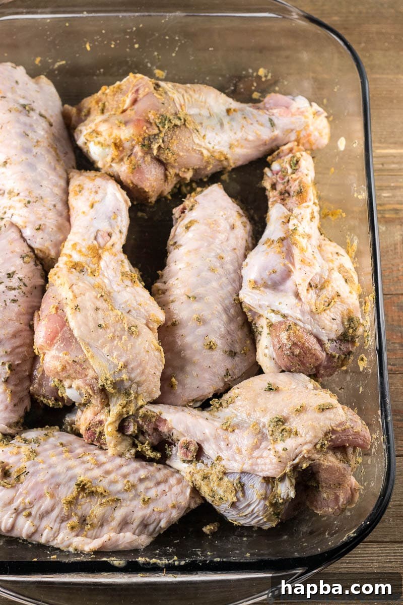 Raw turkey wings generously seasoned with a savory herb and spice blend, neatly arranged in a glass baking dish, ready for the oven.
