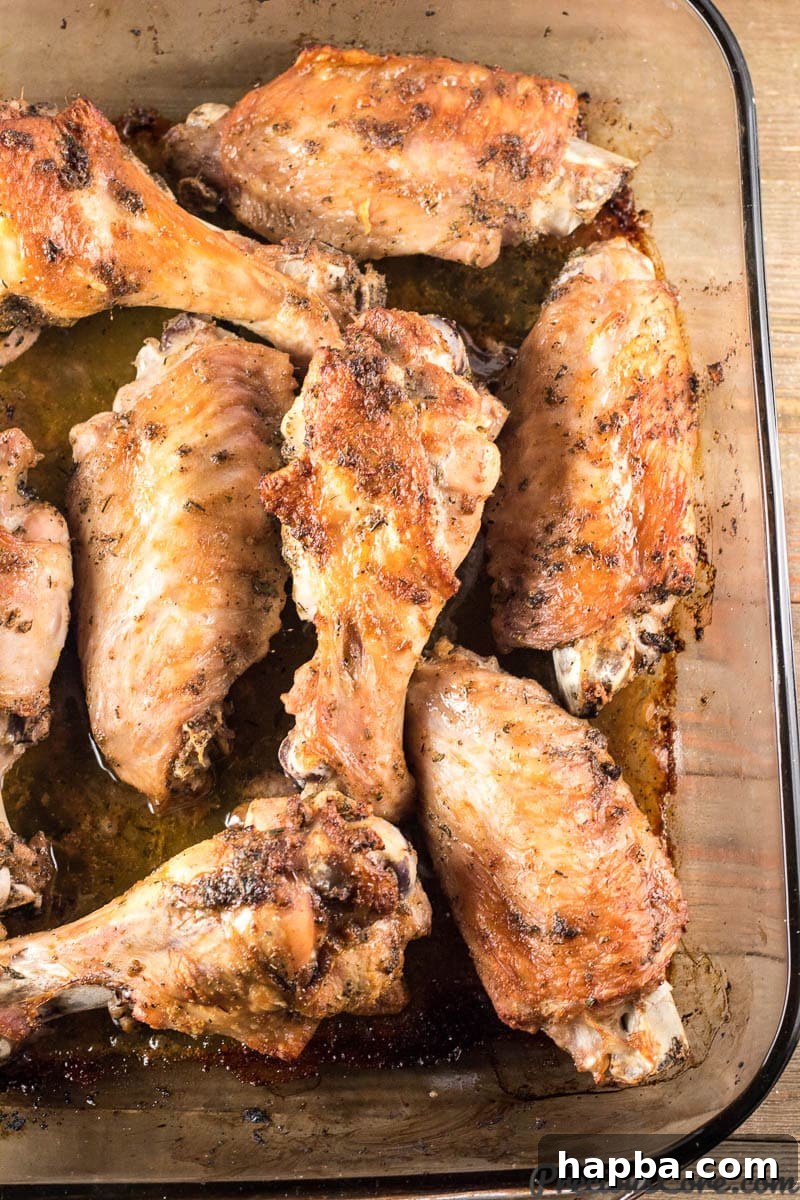 Partially baked turkey wings showcasing developing golden-brown skin, simmering in their own juices within a glass baking dish.