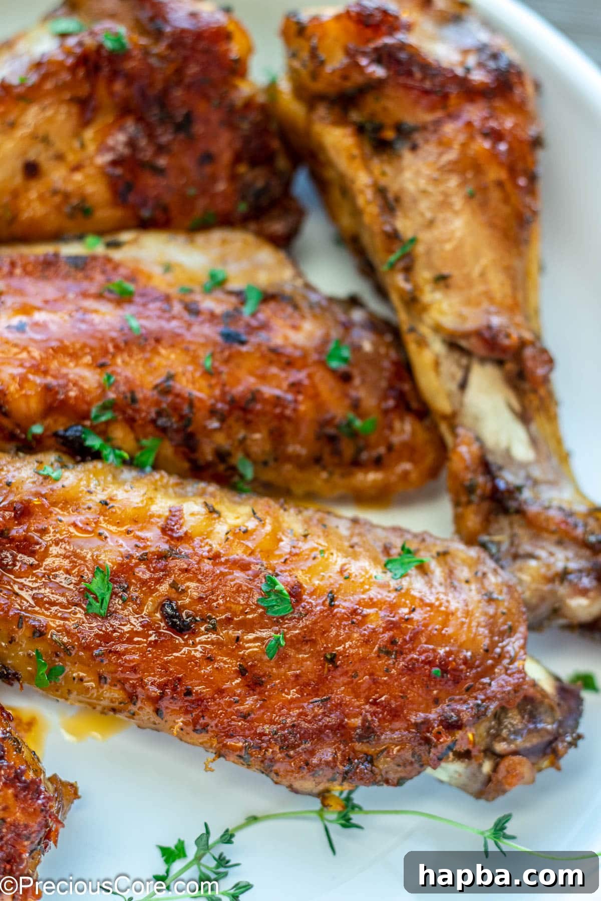 Brown cooked turkey wings beautifully garnished with fresh minced parsley, enhancing their appetizing appearance on a white background.