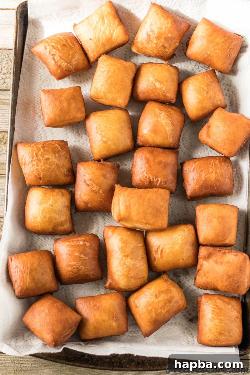 Big Easy Beignets 7 Freshly fried, golden brown beignets draining on a wire rack over paper towels.