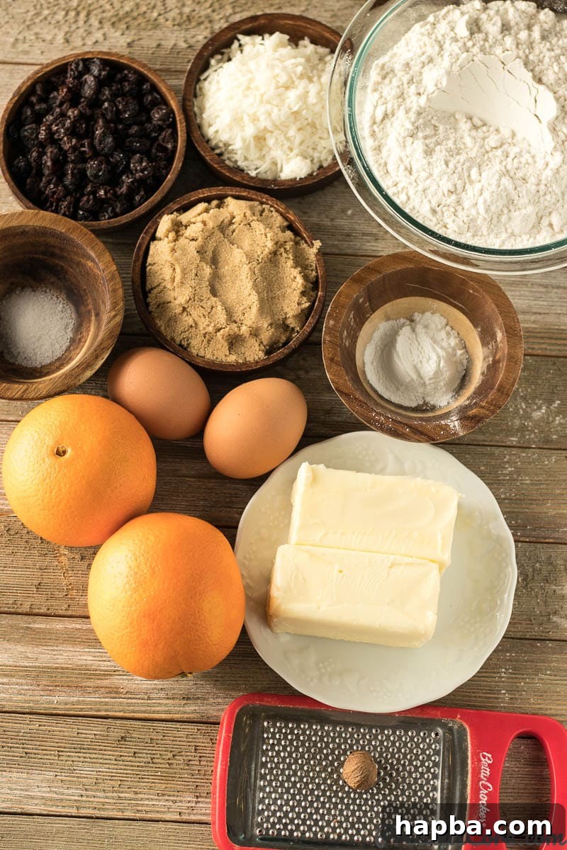 Various ingredients for Christmas Fruit Cake recipe, including flour, butter, eggs, oranges, raisins, and shredded coconut, neatly arranged on a kitchen counter.