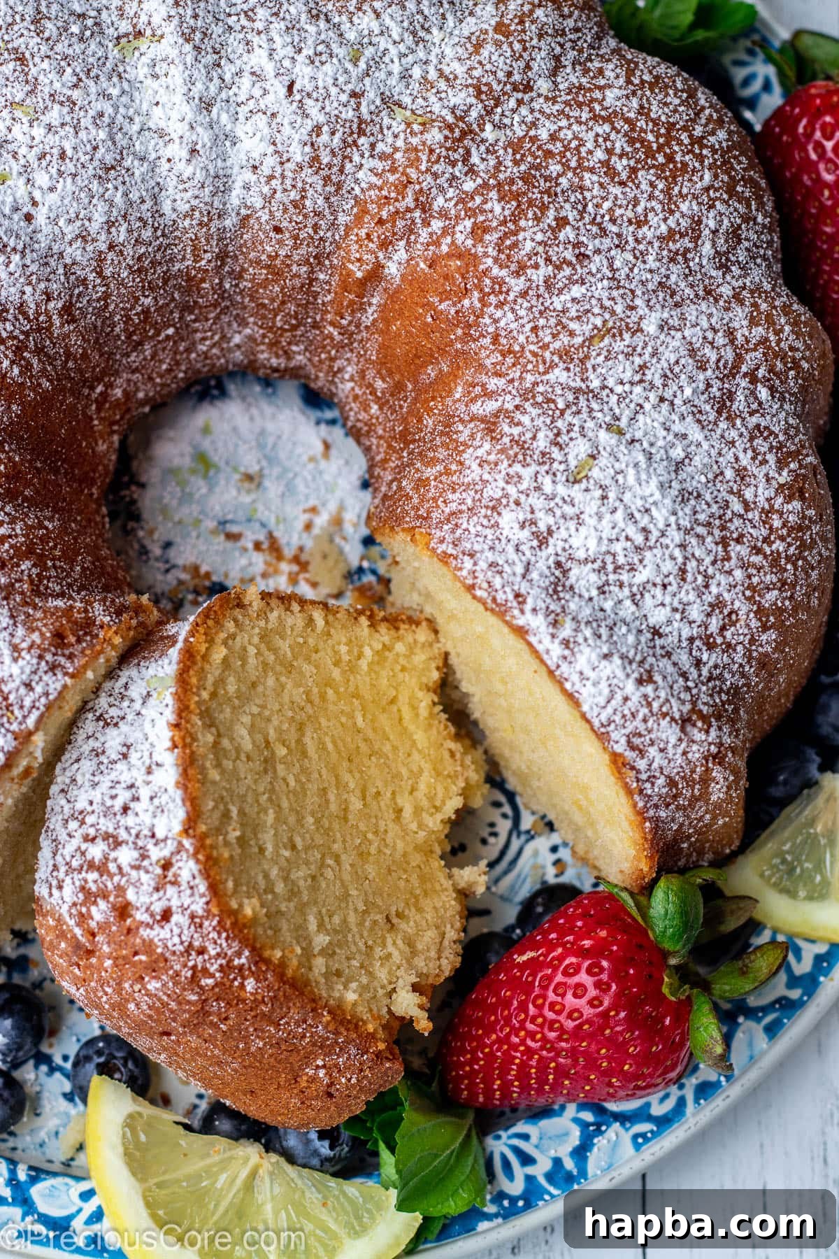 A beautifully sliced lemon pound cake on a round platter, showcasing its moist crumb. A piece has been cut out, ready to be served.