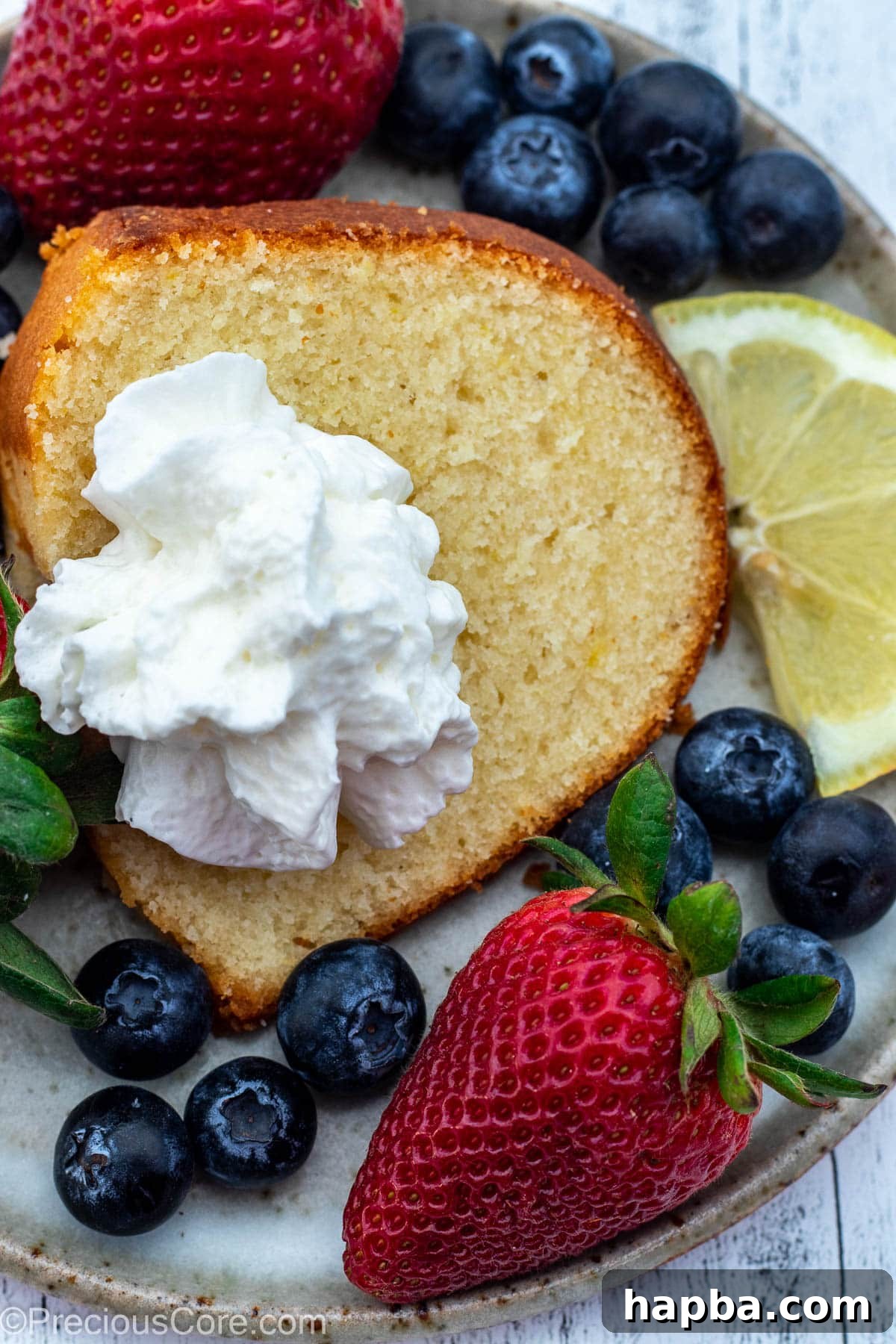A delightful slice of moist lemon pound cake on a white plate, adorned with a cloud of whipped cream and vibrant fresh berries.