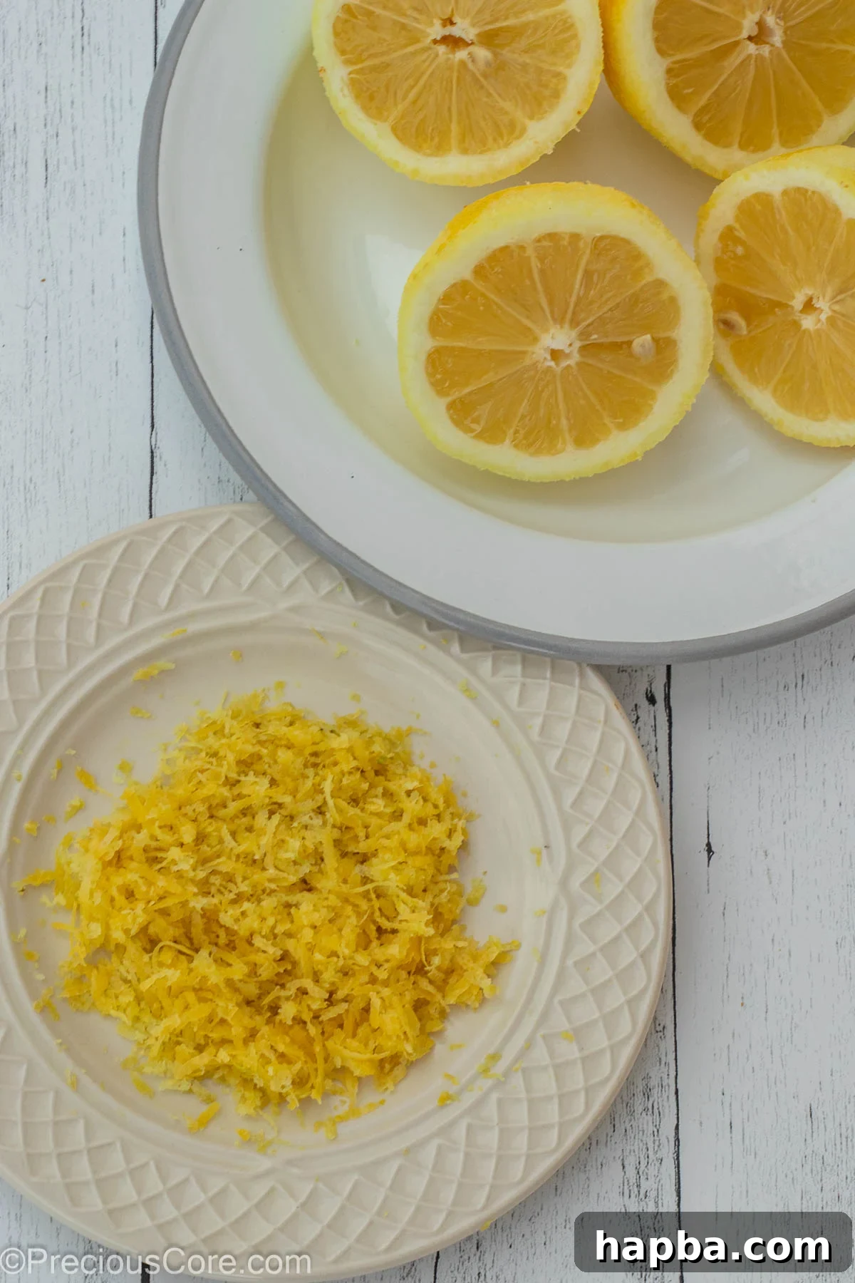 Lemon zest carefully grated onto one plate, with fresh lemon halves ready for juicing on another plate, highlighting the two forms of lemon used.