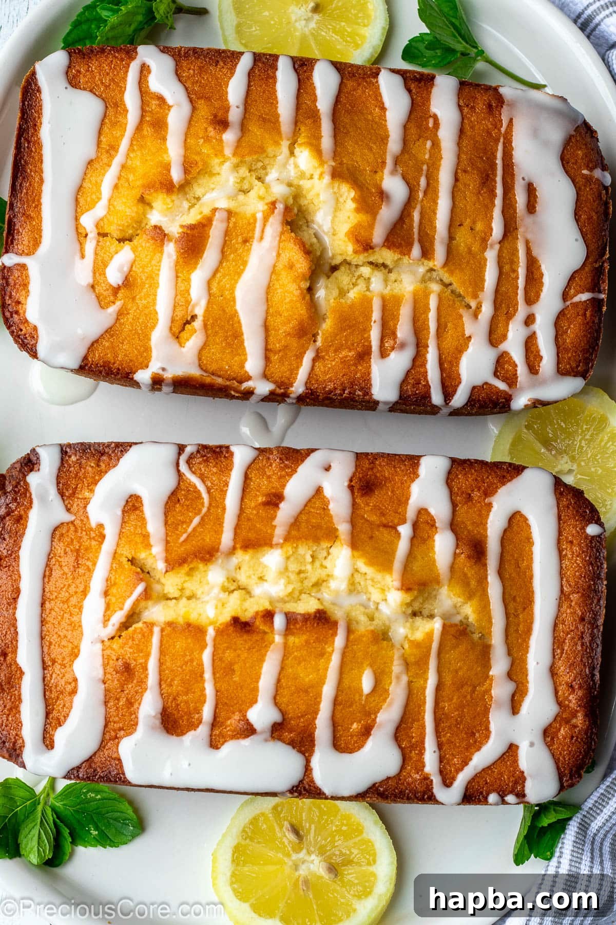 Two golden-brown loaf cakes, each generously drizzled with a shiny lemon glaze, ready for serving.