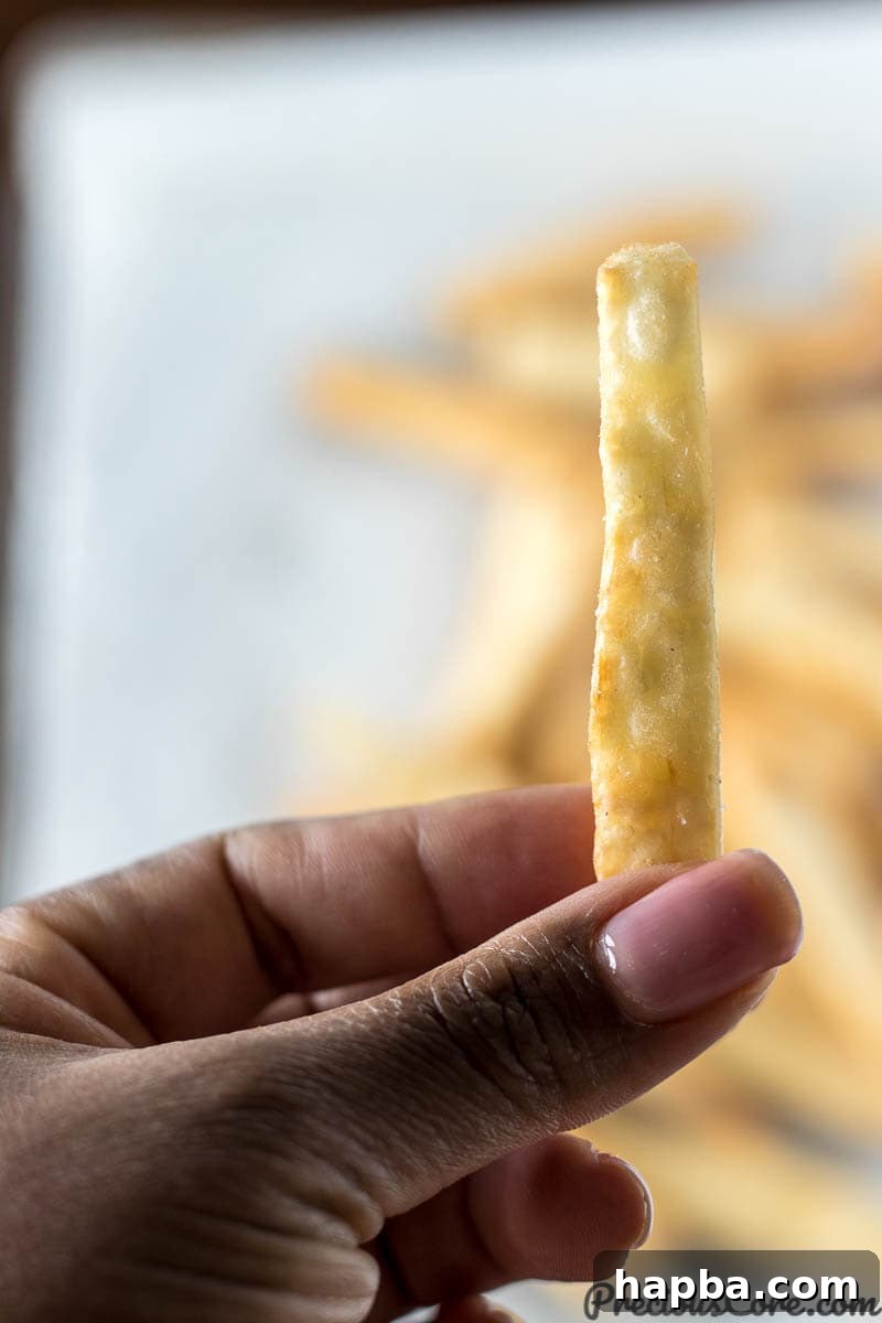 Hand holding a crispy yuca fry, showing its appealing texture.