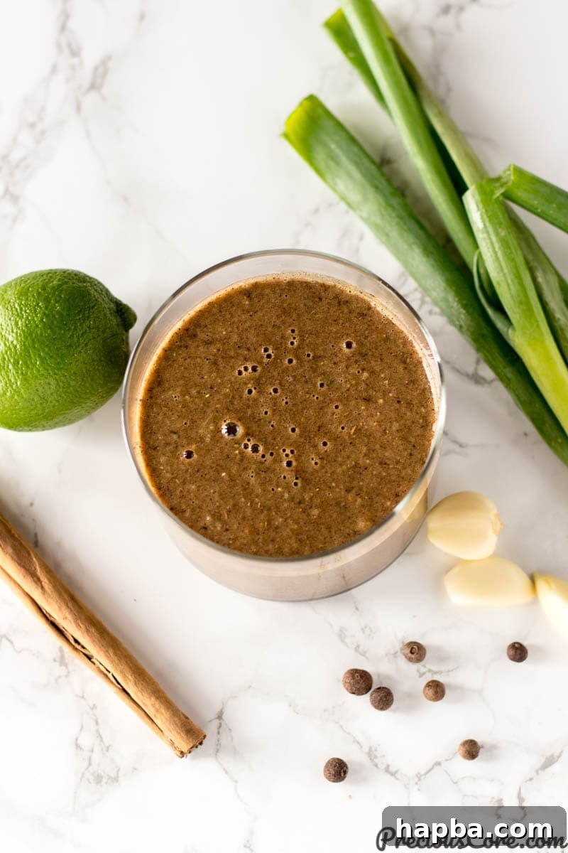 Glass of Jamaican jerk seasoning surrounded by ingredients such as garlic and lime.