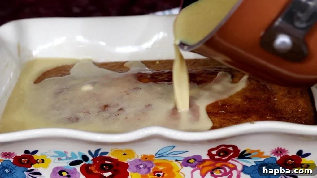 A rich, buttery sauce being carefully poured from a saucepan over a freshly baked Malva Pudding cake, ensuring even absorption.