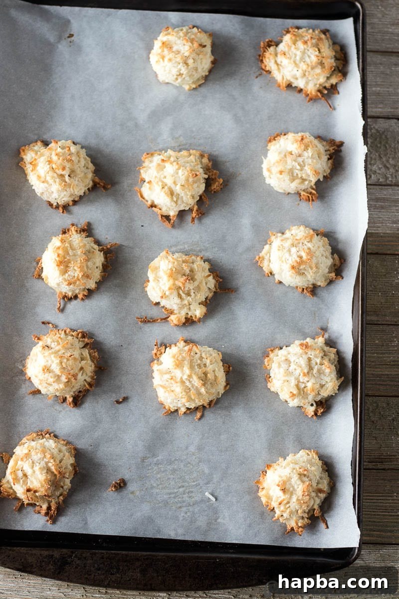 Effortless Coconut Macaroons 3 Freshly baked easy coconut macaroons, golden and slightly browned around the edges, cooling on a parchment-lined baking sheet.