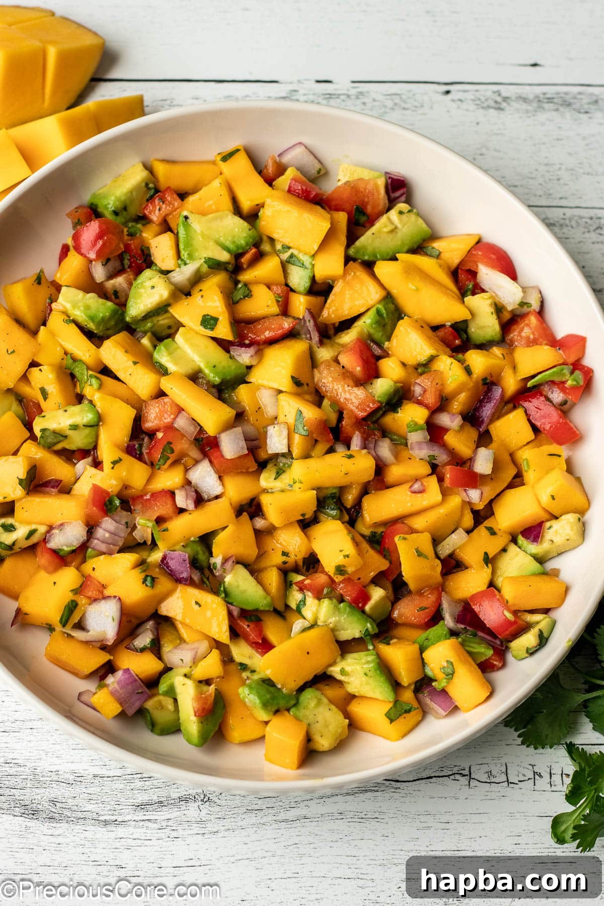 A bowl with diced mango, avocado, and other ingredients for salsa.
