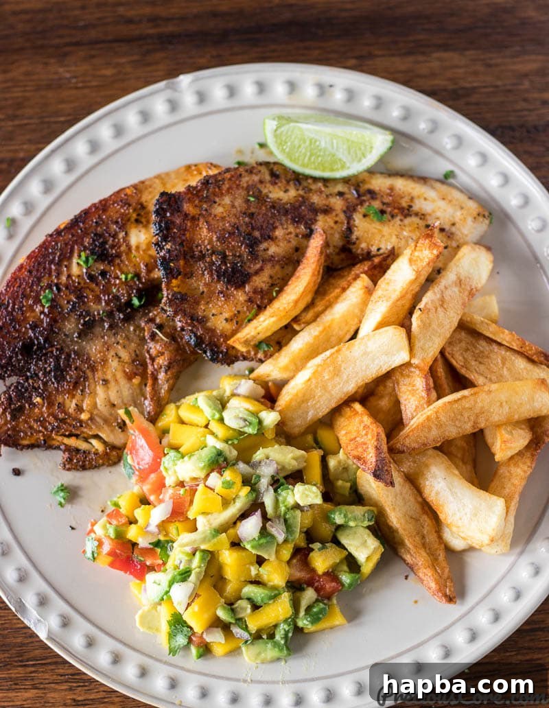 Grilled fish, a lime wedge, and a generous portion of mango avocado salsa on a plate.